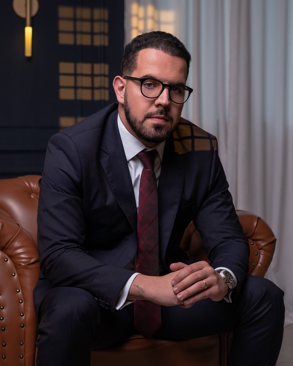 Pedro Berenguer dos Santos, advogado, sentado em uma poltrona de couro, de terno escuro e gravata vinho