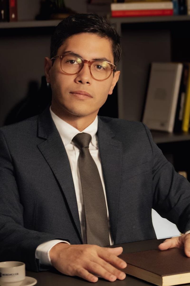 Renan Antonio Soares Domingues, advogado, sentado à mesa com um livro, de terno escuro e óculos